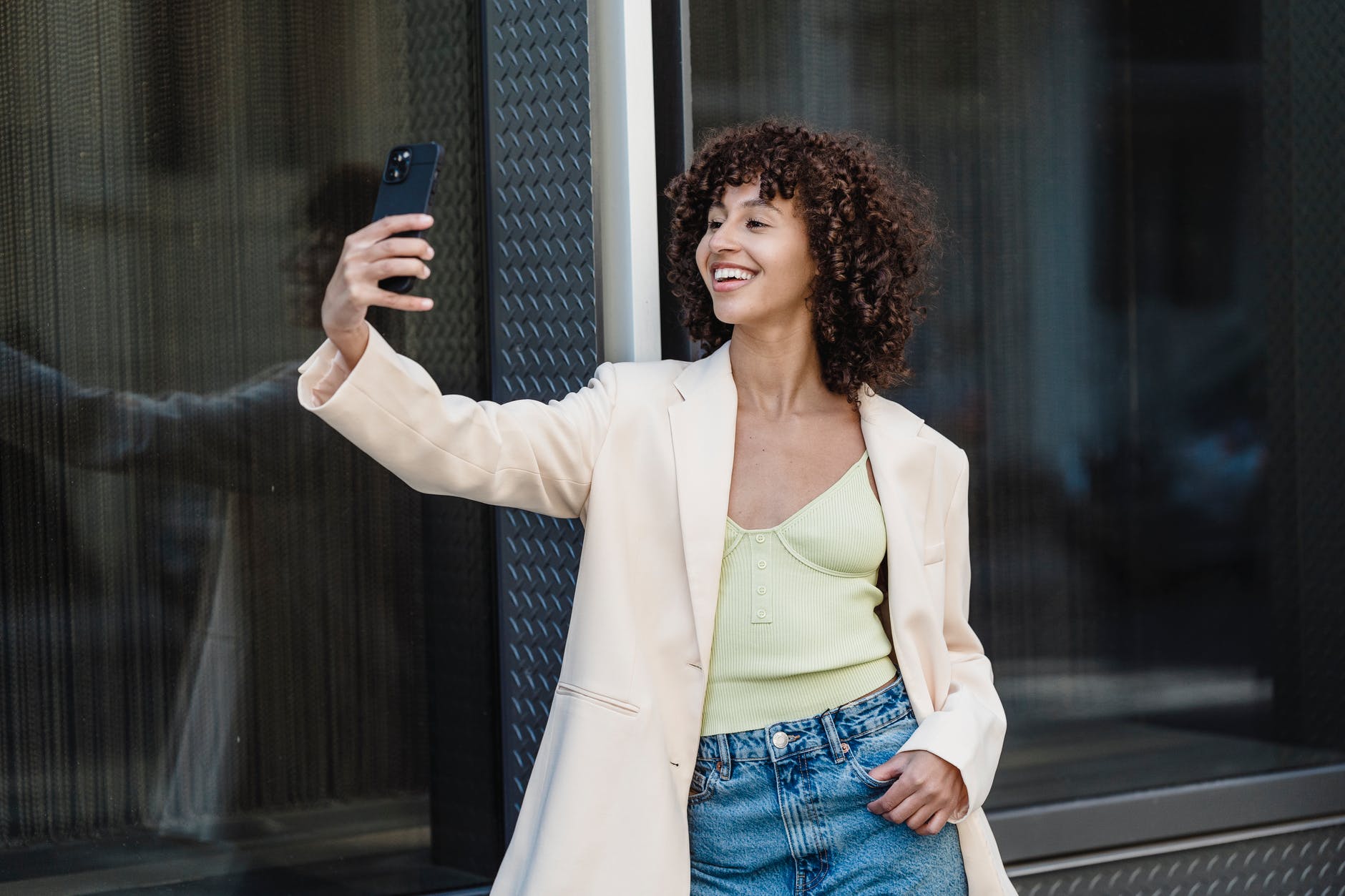 positive ethnic woman taking self portrait on smartphone in town