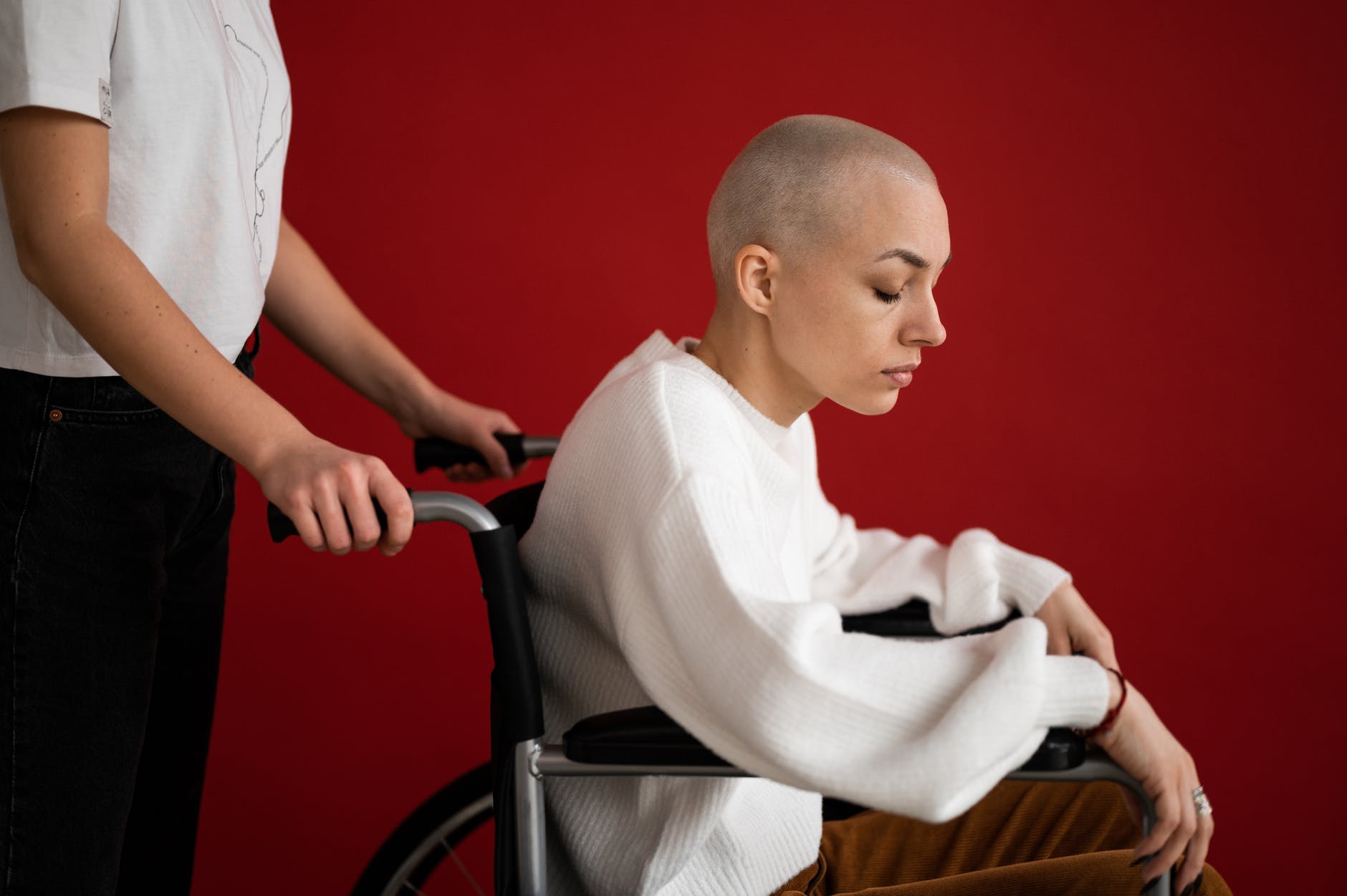 crop assistant pushing wheelchair with sick patient on red background