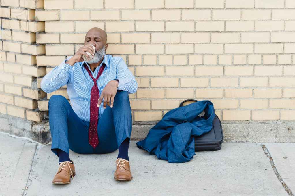 senior beard black man in office costume sitting on ground