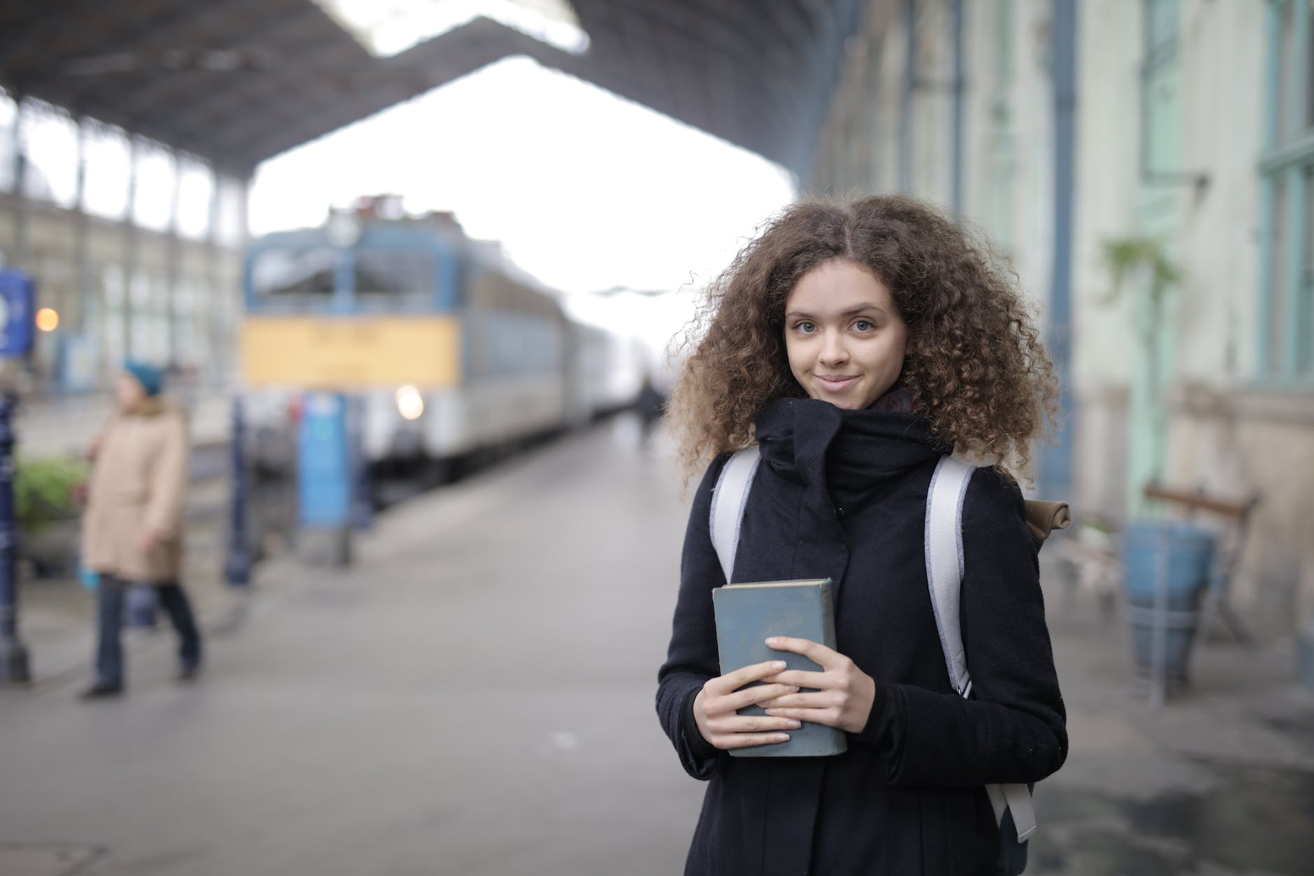 positive young lady with backpack and book standing on platform