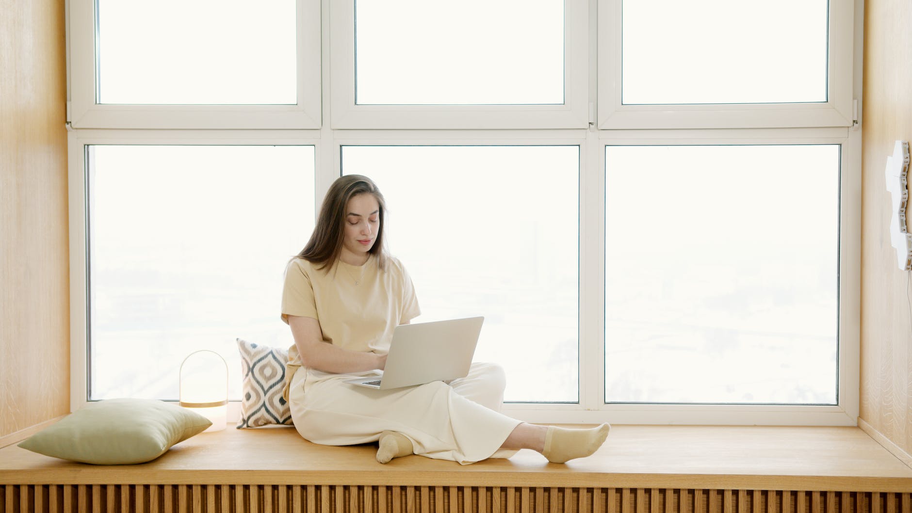 a woman sitting on a windowsill while using typing on her laptop