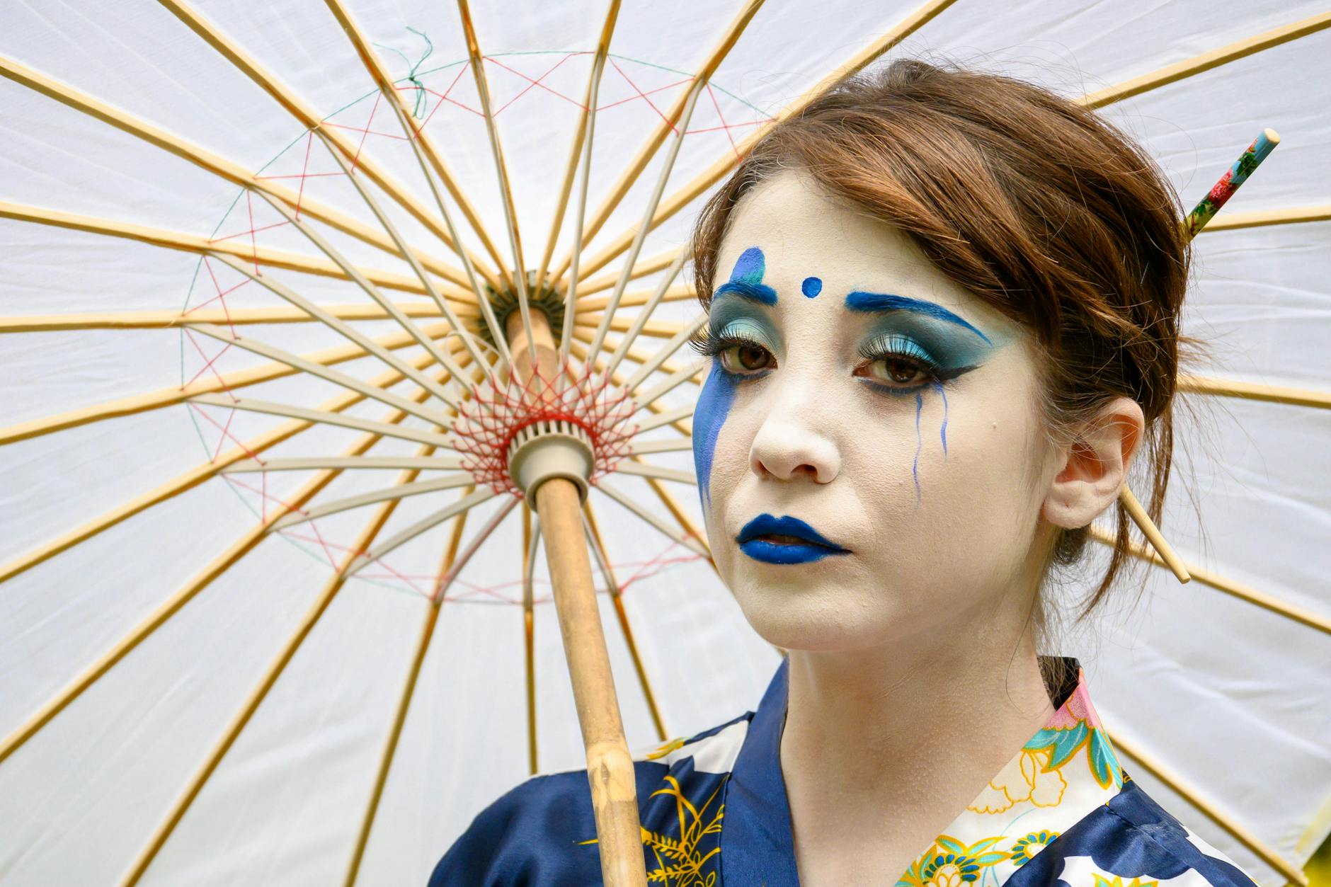 a woman with blue face paint holding a white umbrella