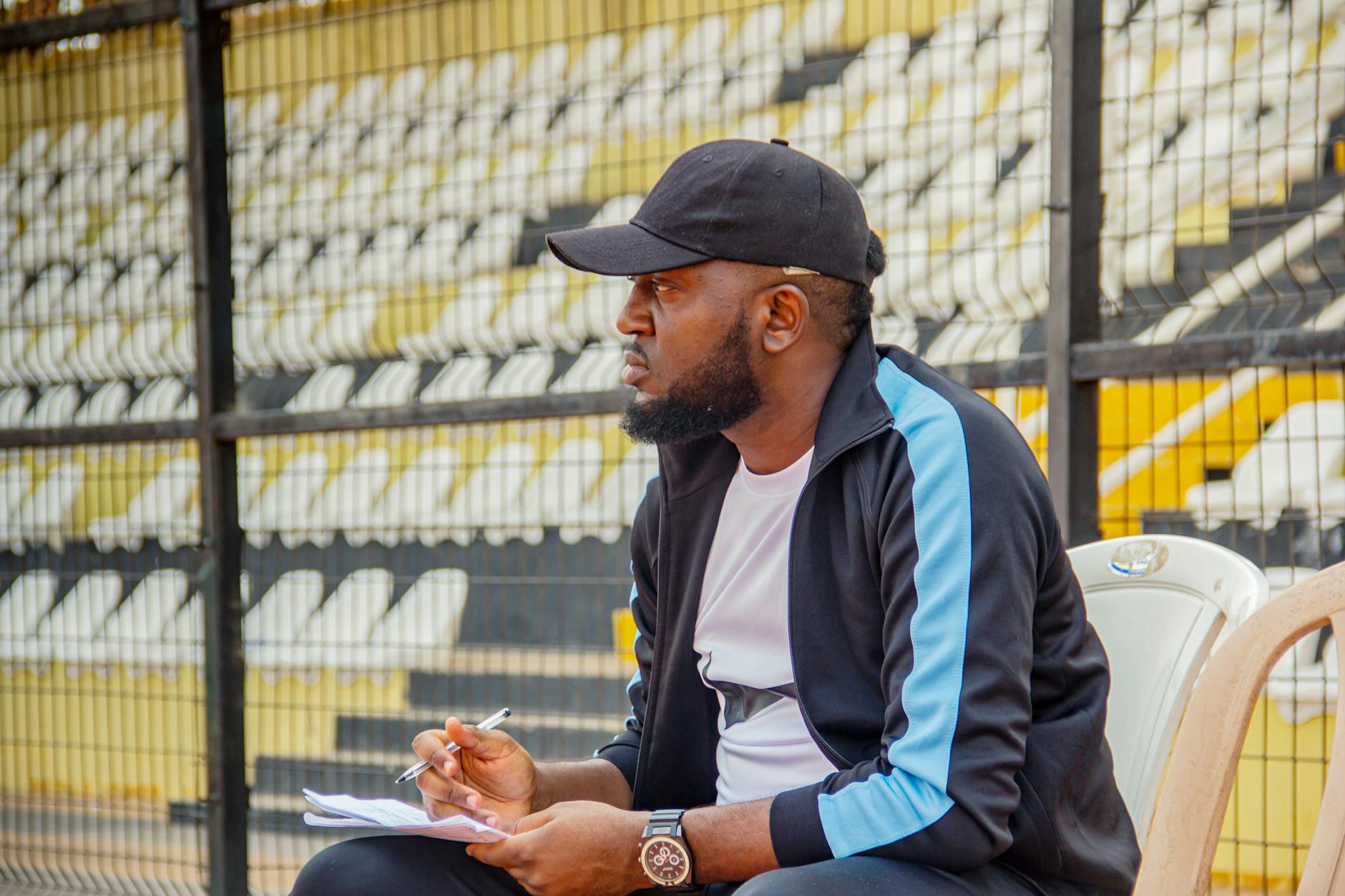 man in cap sitting and taking notes at stadium