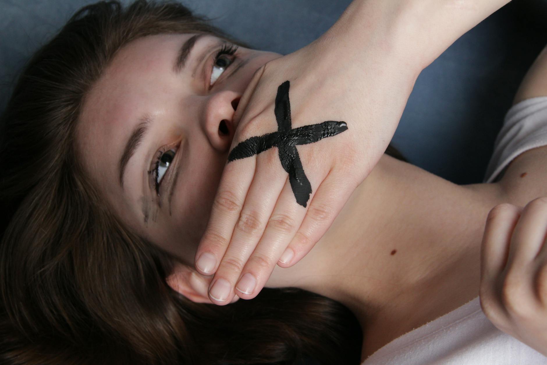 woman lying on her back covering her mouth with a marked hand