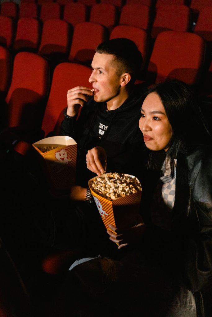 man and woman eating popcorn while sitting in a cinema