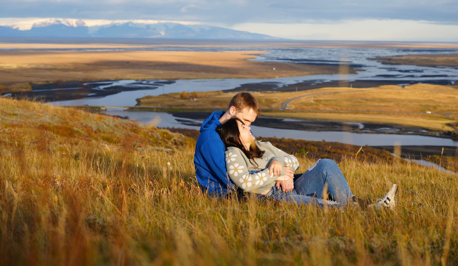a couple sitting on a hill overlooking a river