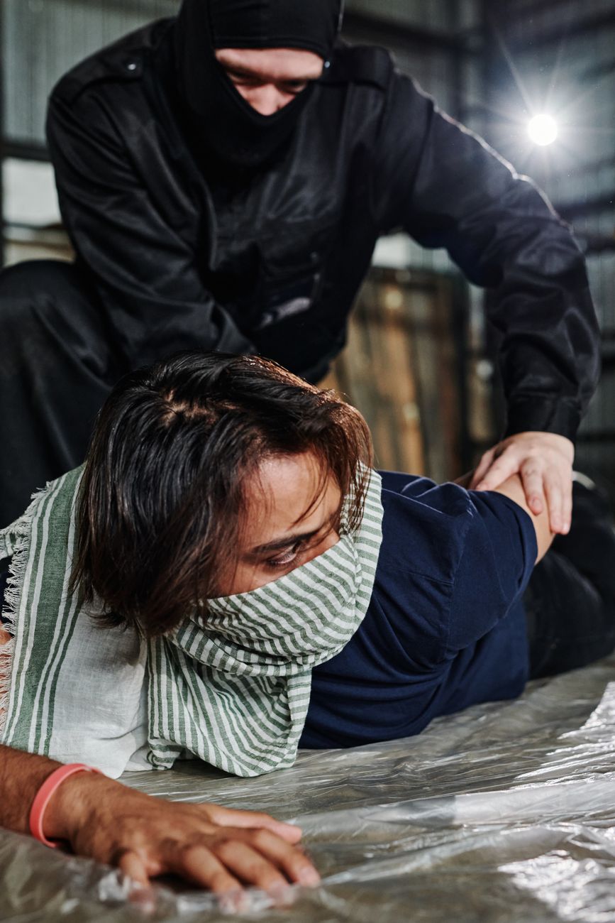 a man in black balaclava twisting the arm of the person lying on the ground