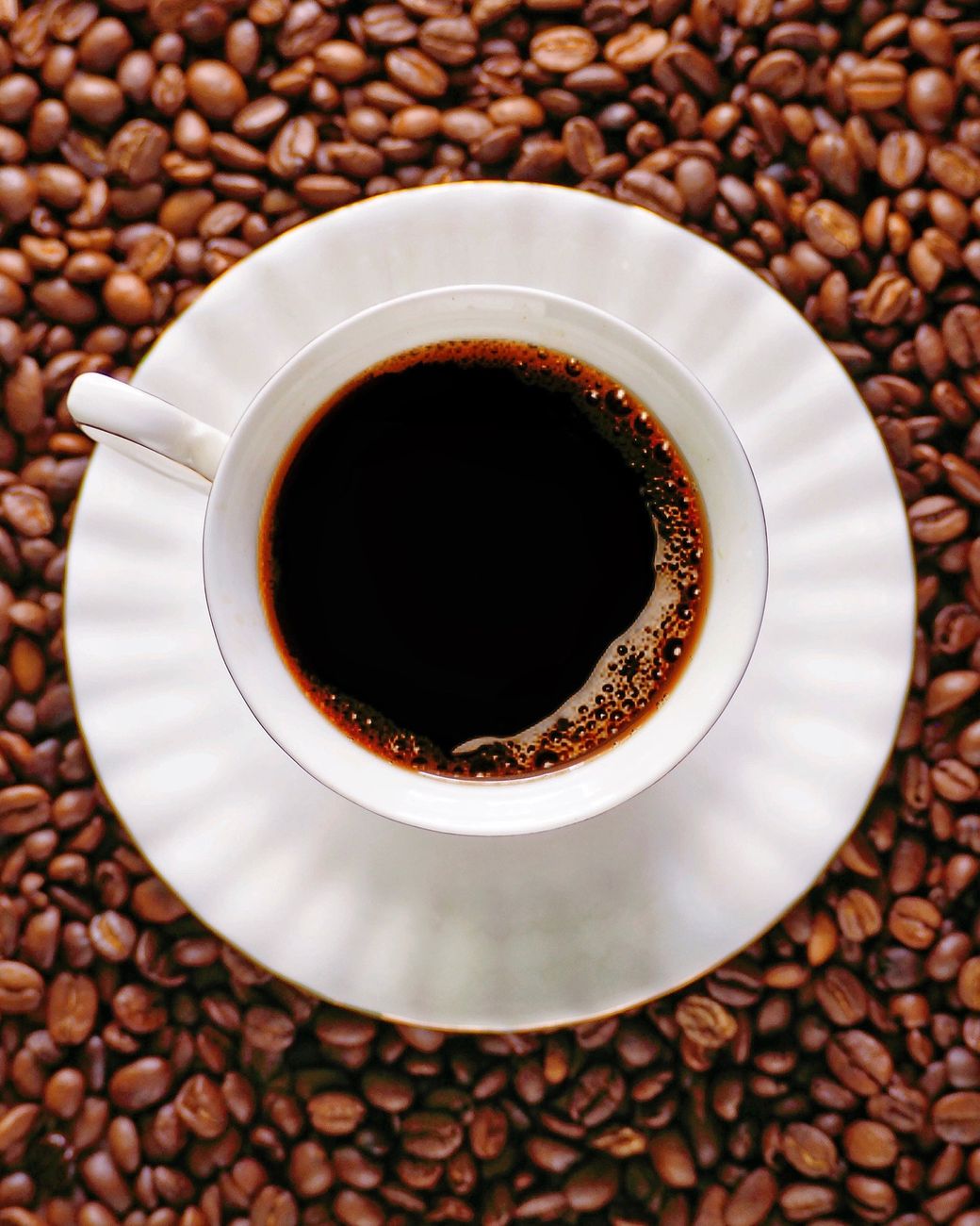 black coffee on white cup with saucer on top of coffee beans